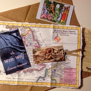 May include: A vintage map of England with a book titled "The Were-Wolf" by Clemence Housman, a small postcard with a wolf illustration, and a pamphlet titled "The Wolf Pack: Perfect reproductions from the legendary illustrations and landscapes of Europe."