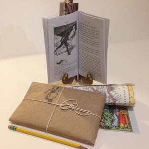 May include: A brown paper package tied with twine, a yellow pencil, and a rolled up map with the text "WESTPHALIA" visible. A small book with a black and white illustration of a person in a historical costume is on a gold metal stand.