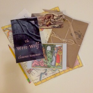 May include: A brown paper envelope with a string tied around it. The envelope is on top of a map with a book titled "The Were-Wolf" by Clemence Housman. There is a small card with a picture of a wolf and people in a forest.