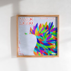 May include: A framed poster with a colorful abstract design. The poster features a silhouette of a person's head with a colorful, spiky design behind it. The text "Panic! At The Disco" and "Behind The Sea" are printed on the poster.
