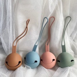 May include: Four silicone baby teethers in different colors: brown, blue, pink, and green. Each teether has a smiley face design and a loop for attaching to a stroller or diaper bag.