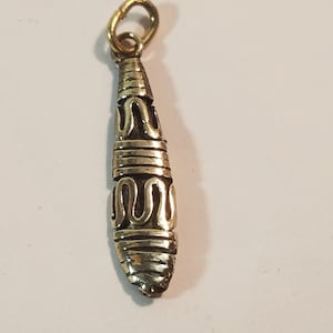 Könnte beinhalten: Ein goldfarbener Anhänger mit einem detaillierten, komplizierten Design. Der Anhänger ist oval geformt, lang und dünn, mit einer Öse oben zum Anbringen an einer Kette.