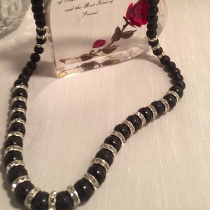 May include: Black lava rock and crystal bead necklace with a silver clasp. The necklace is displayed on a clear heart-shaped stand with a dried red rose inside. The stand has the text "My Mother A Listener, Teacher and Miraculous Blend of Peacemaker, Counselor and the Best Kind of Friend".
