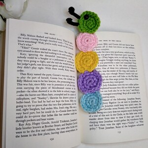 May include: A colorful crocheted caterpillar bookmark with a black pipe cleaner antenna. The bookmark is on top of an open book with text about a trial.