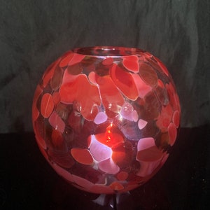 May include: A red glass bowl with a speckled pattern of white, pink, and red. The bowl is round and has a smooth, glossy finish.