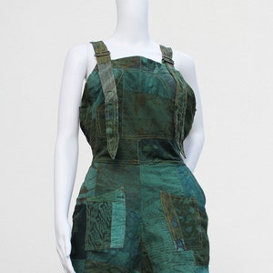 May include: Green patchwork dungarees with adjustable straps. The dungarees are made of a variety of fabrics with a green and brown pattern.