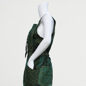 Può includere: Un vestito di tuta verde in patchwork con un laccio in vita. Il vestito presenta una varietà di motivi floreali e geometrici.