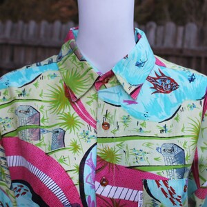 May include: A colorful button-down shirt with a green, blue, pink, and white abstract pattern. The shirt has a collar and a button-up front.