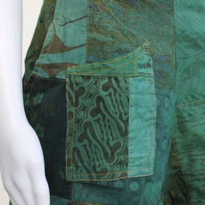 May include: Close-up of a green patchwork skirt with a large pocket on the front. The pocket is made of a different fabric with a swirling pattern.