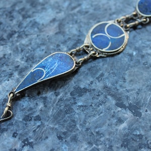 May include: A silver chain bracelet with three blue lapis lazuli stones. The stones are set in silver and have intricate designs. The bracelet has a hook clasp.