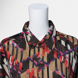 Può includere: Una camicia abbottonata con motivo geometrico nero, marrone, rosso e blu.