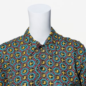 Può includere: Una camicia abbottonata con colletto a motivo blu, verde, rosso e giallo. Il motivo presenta un design ripetitivo di un giglio stilizzato.