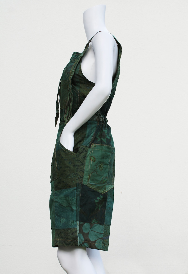 May include: A green patchwork overall dress with a tie at the waist. The dress features a variety of floral and geometric patterns.