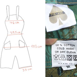 May include: A black and white line drawing of a pair of dungarees with measurements in centimetres. The dungarees have two pockets on the front. The image also shows a green fabric with a white label that says "PIK-ASS" and a white label with care instructions that says "100% COTTON COLD WASH OR DRY CLEAN".
