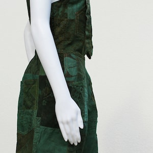 May include: A green patchwork jumpsuit with a sleeveless top and shorts. The fabric has a dark green base with a lighter green pattern.