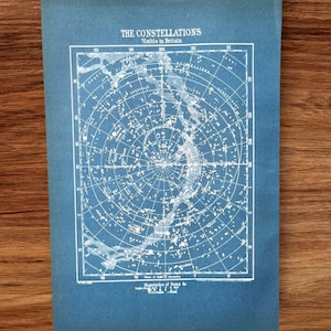 Könnte beinhalten: Ein blauer Druck der in Großbritannien sichtbaren Sternbilder. Der Druck zeigt eine detaillierte Sternenkarte mit weißen Linien und Text, einschließlich des Titels "The Constellations" und "Visible in Britain". Der Druck hat einen blauen Hintergrund.