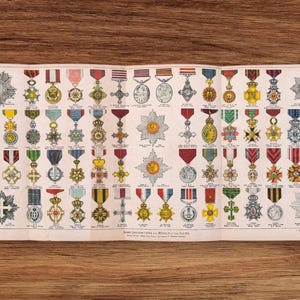 May include: A vintage print displaying a variety of medals and awards, each with a unique design and colour scheme. Ribbons in red, blue, green, and yellow are attached to the medals. The print is on aged paper, showing detailed illustrations.