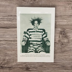 May include: A monochrome vintage photograph showing a person in a striped prison uniform, seated in a chair with their hair standing on end. The number "130013" is visible. The text at the bottom reads "Enjoying a 30,000 Volt Charge of Electricity."