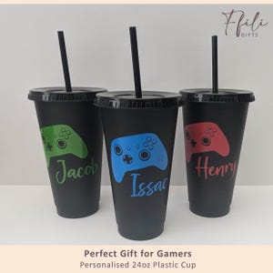 May include: Three black plastic cups with lids and straws, each with a video game controller design in green, blue, and red. The cups are personalised with names. Each cup holds approximately 710ml.