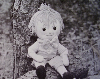 May include: A handmade rag doll with yarn hair, wearing a checkered shirt and a bow tie, sitting on a tree trunk.