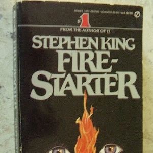 May include: A paperback book titled "Fire-Starter" by Stephen King. The cover is black with the title in large white letters. The image features a flame design with two eyes.