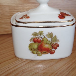 May include: White ceramic sugar bowl with a lid. The bowl has a gold trim and a fruit design with pears, apples, and berries.