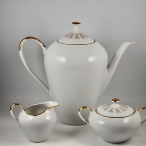 May include: A white porcelain tea set with gold trim. The set includes a teapot, creamer, and sugar bowl.