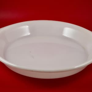 May include: White ceramic pie plate with a slightly rounded rim and two small handles on the sides.
