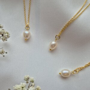 Dainty pearl necklaces on 18k gold plated chains on a soft white fabric background surrounded by flowers