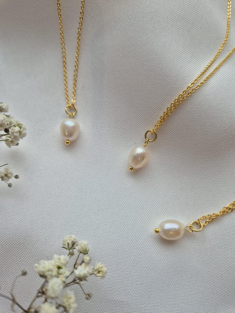 Dainty pearl necklaces on 18k gold plated chains on a soft white fabric background surrounded by flowers