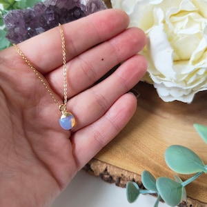 May include: A delicate gold chain necklace with a small, round, light blue and white gemstone pendant.
