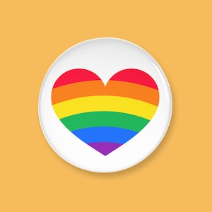 May include: A white, round button with a rainbow heart design. The heart features horizontal stripes in red, orange, yellow, green, blue, and purple. The button is set against a solid orange background.