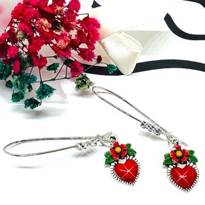 Peut inclure: Une paire de boucles d'oreilles pendantes argent&eacute;es avec des breloques en forme de c&oelig;ur rouge. Chaque breloque en forme de c&oelig;ur a une fleur rouge avec un centre jaune et des feuilles vertes. Les boucles d'oreilles ont des accents de cristal transparent.
