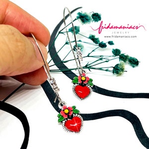 Peut inclure: Une paire de boucles d'oreilles cr&eacute;oles argent&eacute;es avec un pendentif en forme de c&oelig;ur rouge et un motif de fleurs vertes et roses. Les boucles d'oreilles sont d&eacute;cor&eacute;es de strass transparents.