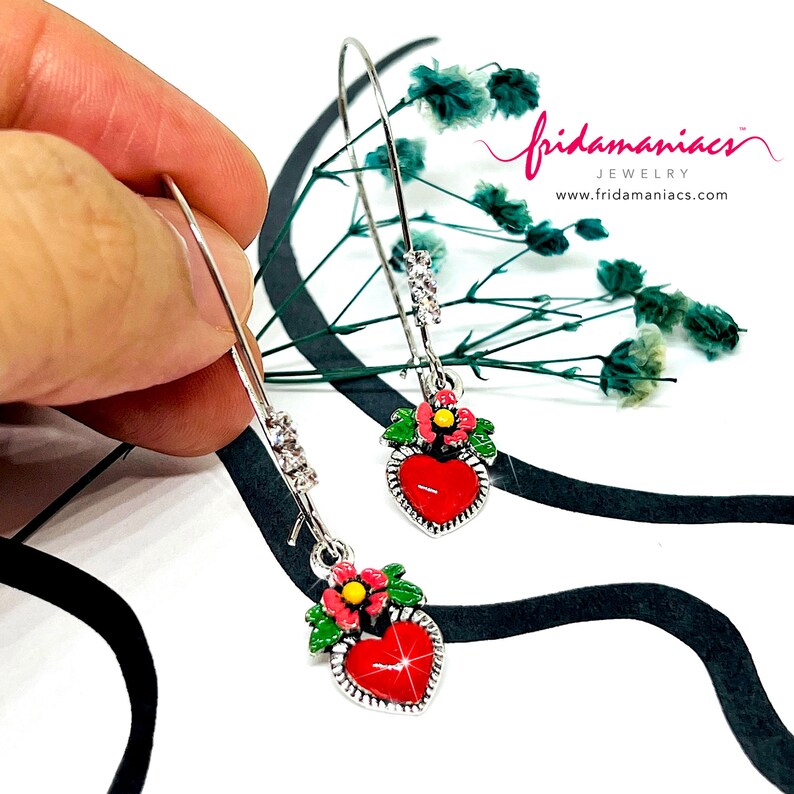Peut inclure: Une paire de boucles d'oreilles cr&eacute;oles argent&eacute;es avec un pendentif en forme de c&oelig;ur rouge et un motif de fleurs vertes et roses. Les boucles d'oreilles sont d&eacute;cor&eacute;es de strass transparents.