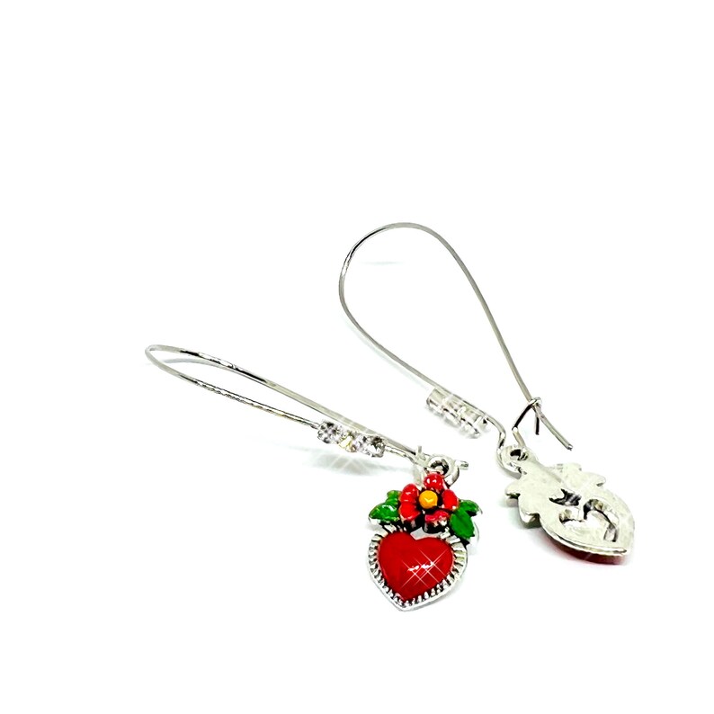 Peut inclure: Une paire de boucles d'oreilles pendantes argent&eacute;es avec un charme en forme de c&oelig;ur rouge. Le charme en forme de c&oelig;ur a une fleur verte avec un centre jaune. Les boucles d'oreilles ont des accents de cristal transparent.