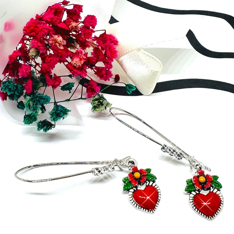 Peut inclure: Une paire de boucles d'oreilles pendantes argent&eacute;es avec des breloques en forme de c&oelig;ur rouge. Chaque breloque en forme de c&oelig;ur a une fleur rouge avec un centre jaune et des feuilles vertes. Les boucles d'oreilles ont des accents de cristal transparent.