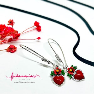 Peut inclure: Une paire de boucles d'oreilles pendantes argent&eacute;es avec des breloques en forme de c&oelig;ur rouge. Chaque breloque en forme de c&oelig;ur a une fleur verte et rouge avec un centre jaune.