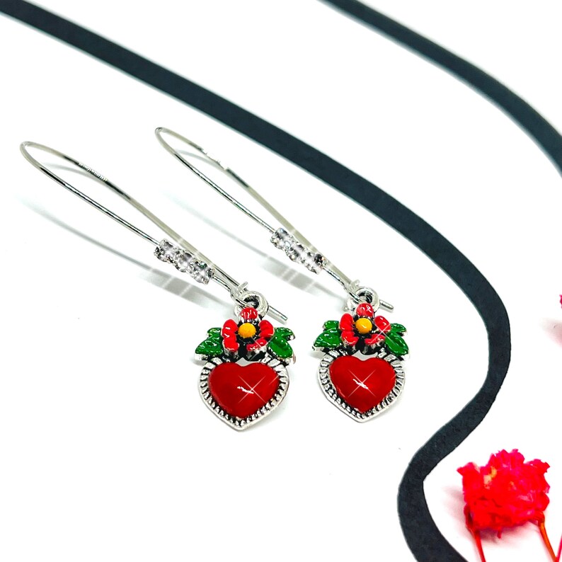Peut inclure: Une paire de boucles d'oreilles pendantes argent&eacute;es avec des breloques en forme de c&oelig;ur rouge. Chaque breloque en forme de c&oelig;ur a une feuille verte et une fleur rouge avec un centre jaune.