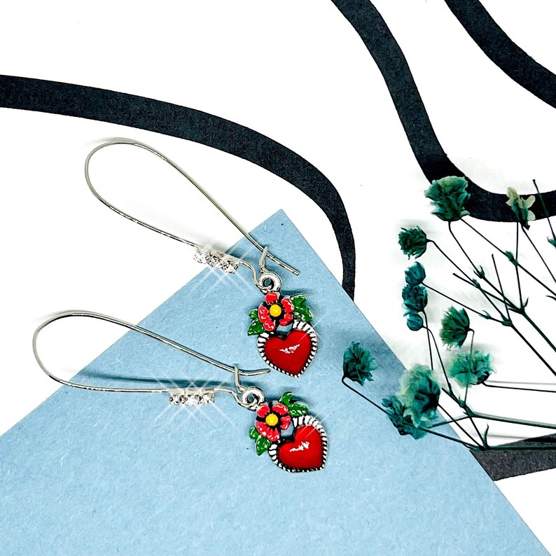 Peut inclure: Une paire de boucles d'oreilles pendantes argent&eacute;es avec des breloques en forme de c&oelig;ur rouge et une seule fleur rouge avec des feuilles vertes. Les boucles d'oreilles ont des accents de cristal transparent.