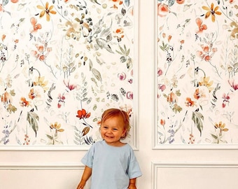 Könnte beinhalten: Ein kleines Kind in einem hellblauen Shirt und rosa Shorts steht vor einer Wand, die mit Blumenmuster-Tapete bedeckt ist. Die Tapete zeigt ein Aquarell-Design in verschiedenen Rosatönen, Gelb und Grün.