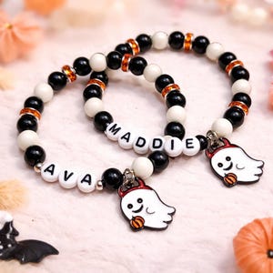 Peut inclure: Deux bracelets de perles avec des perles noires, blanches et orange. L'un des bracelets épelle "AVA" et l'autre "MADDIE" avec des perles de lettres blanches. Chaque bracelet a un charme de fantôme avec une corne de diable et une citrouille.