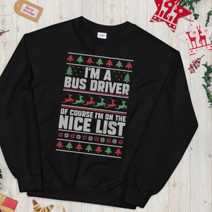 Puede incluir: Sudadera negra con un diseño navideño. El texto dice "I'M A BUS DRIVER OF COURSE I'M ON THE NICE LIST" en blanco y rojo. El diseño incluye árboles de Navidad, renos y copos de nieve.