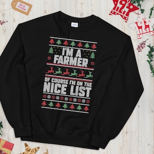 Pode incluir: Camisola preta com um design festivo. O texto "I'M A FARMER OF COURSE I'M ON THE NICE LIST" é exibido em branco, vermelho e verde. O design inclui árvores de Natal, renas e flocos de neve, ideal para a época festiva.