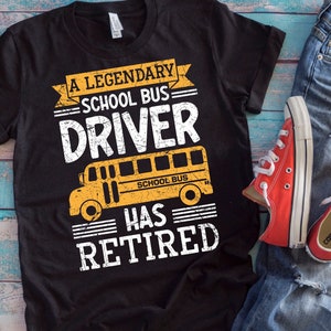 Puede incluir: Una camiseta negra con un gráfico blanco que dice "A Legendary School Bus Driver Has Retired" con una ilustración de autobús escolar amarillo.
