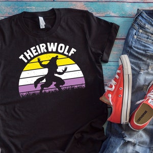 Może przedstawiać: Czarny T-shirt z retro grafiką zachodu słońca i tekstem "THEIRWOLF" w kolorze żółtym. Czarna sylwetka wilkołaka wyjącego do księżyca znajduje się w centrum grafiki. Grafika zachodu słońca ma żółte, białe, fioletowe i lawendowe paski.