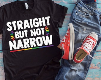 May include: Black t-shirt with the text "Straight but not narrow" in white with a rainbow stripe underneath. The shirt is laid out on a blue wooden surface with a pair of blue jeans and red trainers.