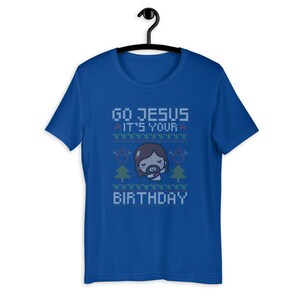May include: Royal blue t-shirt with the text "GO JESUS IT'S YOUR BIRTHDAY" in a pixelated font. The design includes a cartoon Jesus, snowmen, and Christmas trees, creating a festive holiday theme.