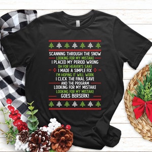Könnte beinhalten: Schwarzes T-Shirt mit einem humorvollen Weihnachtsdesign. Der Text lautet "SCANNING THROUGH THE SNOW, LOOKING FOR MY MISTAKE" und andere lustige Zeilen, mit einem festlichen Muster aus Bäumen und roten Akzenten. Ein einzigartiges Weihnachtsgeschenk.