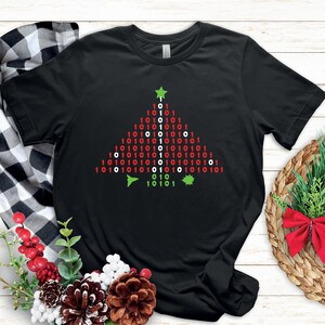 May include: Black t-shirt featuring a green, red and white Christmas tree design made of binary code. The tree has a green star on top and red and green baubles.